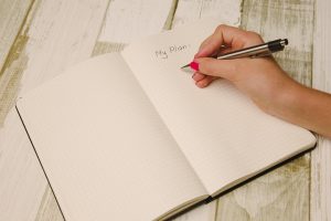 A journal with someone with red nail polish writing in it.
