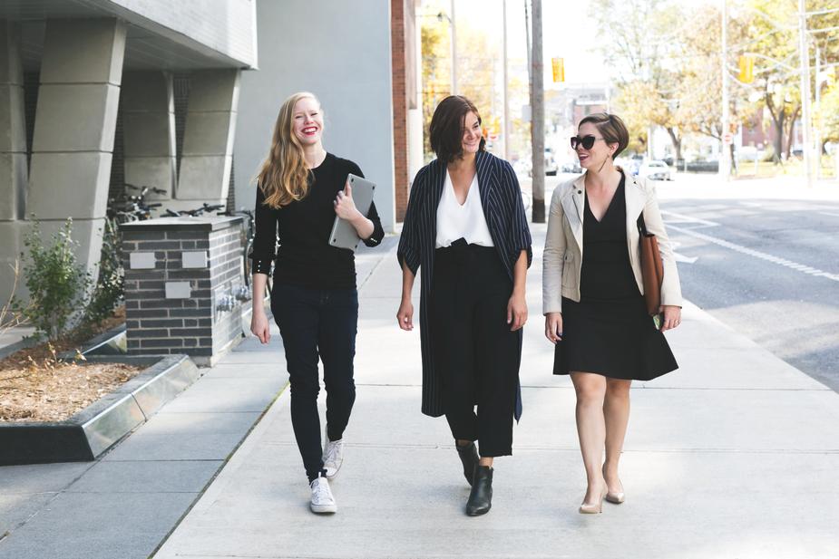 A sidewalk with three woman walking and talking.