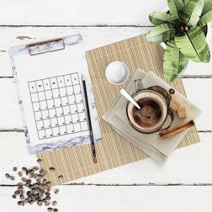 A calendar with a pencil, coffee and a plant on the table.
