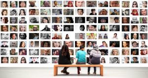 Three people on a bench in front of a mural of faces.